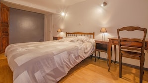 Ein Schlafzimmer mit einem Bett, einem Holzstuhl, einem Schreibtisch und zwei Lampen.