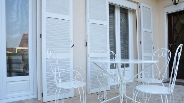 Eine Terrasse mit weißem Metallmöbel, darunter ein Tisch und Stühle, sowie Fensterläden in Weiß.