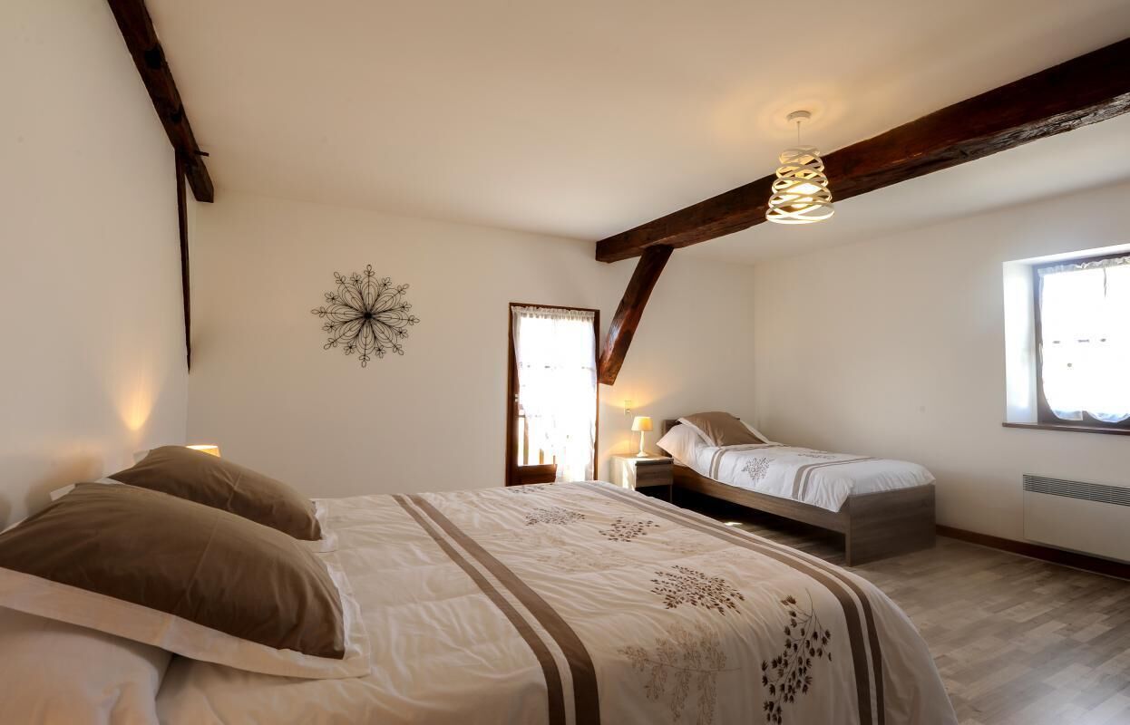 A bedroom with a large bed, a smaller bed, a decorative wall piece, and a window with natural light.