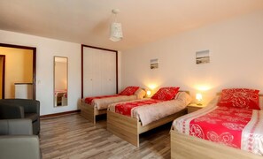 A bedroom with two wooden beds, each with red and white bedding, a wooden floor, a gray sofa, and a white ceiling light.