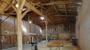 A spacious barn with exposed wooden beams, a brick wall, and a concrete floor.