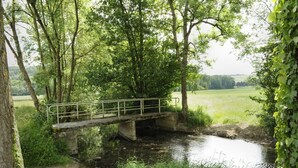 A rustic stone bridge over a narrow stream, surrounded by lush greenery and trees.