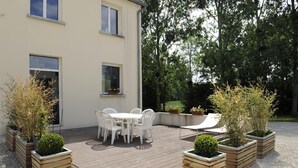 A patio with a wooden deck, white outdoor furniture, and planters with shrubs.
