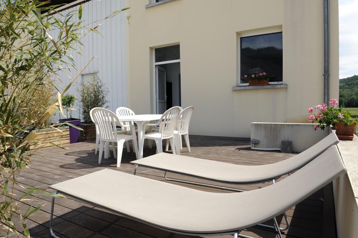 Une terrasse extérieure avec une table et des chaises, un fauteuil de relaxation et des plantes en pot.
