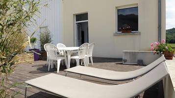 Une terrasse extérieure avec une table et des chaises, un fauteuil de relaxation et des plantes en pot.