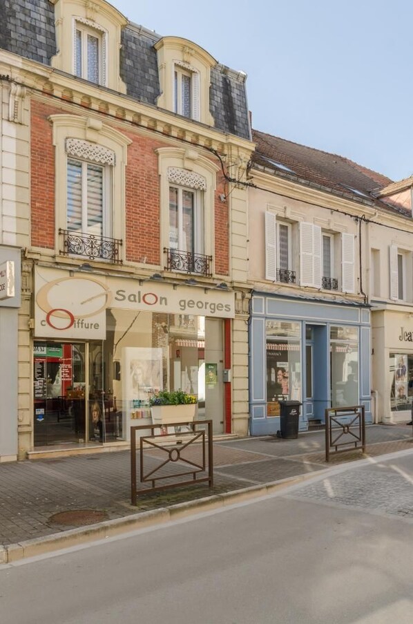 A street view with a building featuring a Salon Georges sign, a storefront with a glass facade, and a blue awning.