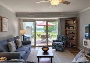 A living room with a sofa, armchair, coffee table, bookshelf, and a television.