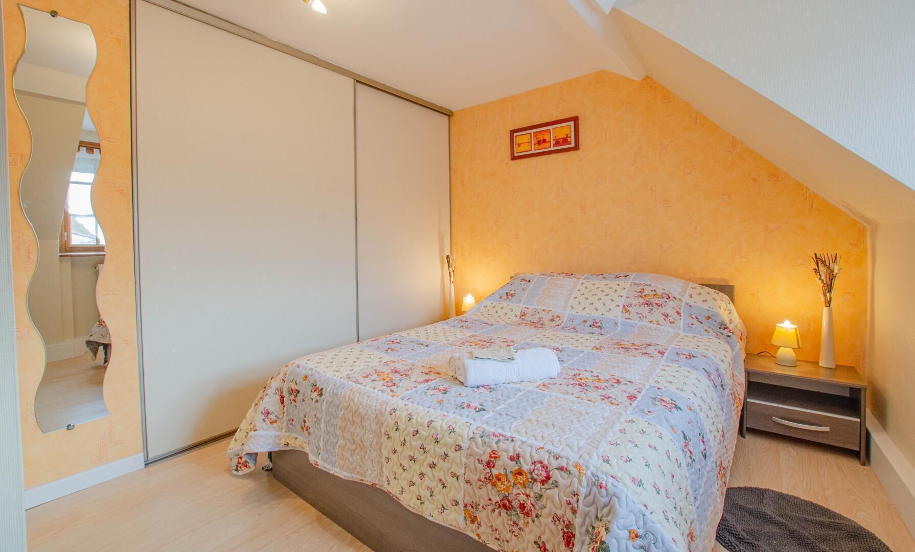 Een slaapkamer met een bed, nachtkastje, lamp en spiegel.