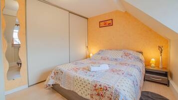 Een slaapkamer met een bed, nachtkastje, lamp en spiegel.