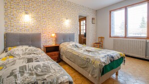 Une chambre avec deux lits, une table de chevet, une chaise, une fenêtre et un radiateur.
