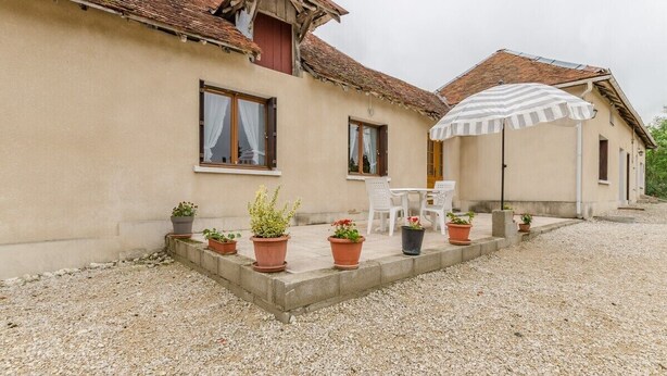 Un bâtiment à la façade beige, doté d’un toit en tuiles et d’une allée en gravier. On y trouve des plantes en pot et du mobilier d’extérieur.