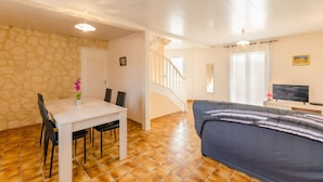A room with a dining table, chairs, a sofa, a TV, and a staircase.