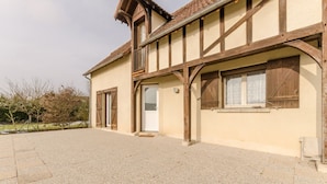 A traditional half-timbered building with a paved courtyard, wooden shutters, and a door.