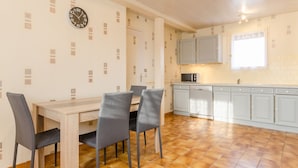 A modern kitchen with a dining area, featuring a wooden table, grey chairs, and light-colored cabinets.