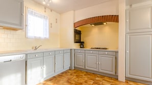 A kitchen with white cabinets, a tiled floor, and a window with a curtain.