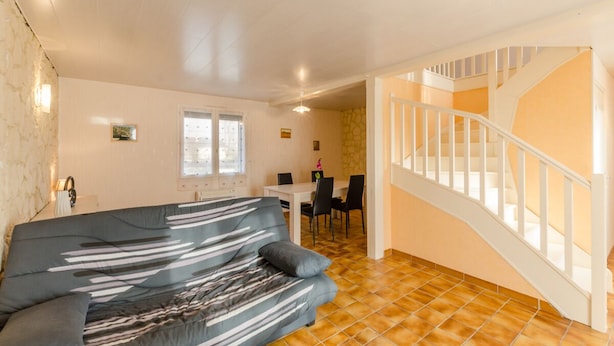 A living room with a sofa, a dining table with chairs, a staircase, and a kitchen area.