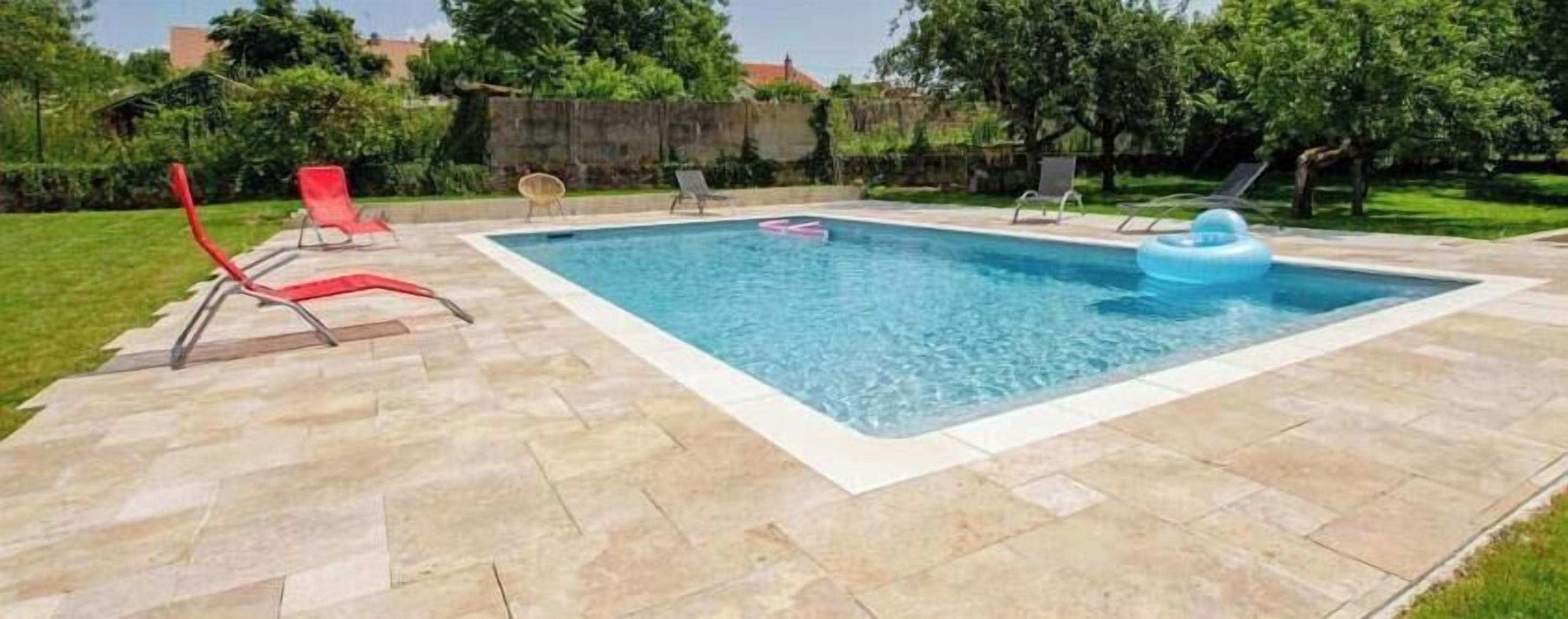 Piscina rectangular con solárium alicatado, rodeada de sillones de descanso y césped.