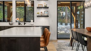 Una cocina moderna con una isla grande, iluminación colgante y vistas a un paisaje nevado a través de amplios ventanales.