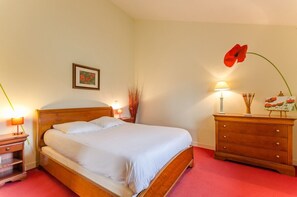 A neatly made bed in a room with a wooden headboard, a bedside table with a lamp, a dresser, and a wall-mounted picture.