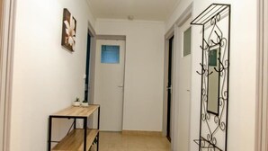 Un pasillo con una lámpara, un banco de madera, un perchero metálico y una puerta al final.