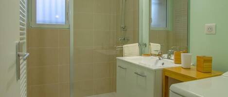 Un baño con ducha, lavamanos, espejo e inodoro.