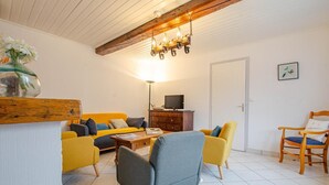Una sala de estar con un sofá, una mesa de centro, una silla de madera y un televisor sobre un mueble.
