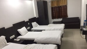A hotel room with three single beds, a dark-colored sofa, a small table with a tray, and a curtain with a pattern. - Hotel Long Stay (Ahmedabad)