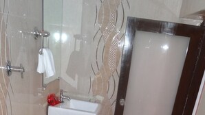 A bathroom with a white sink, a glass shower enclosure, and a door with a frosted glass panel. - Hotel Long Stay (Ahmedabad)