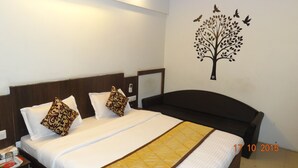 A hotel room with a bed, pillows, a nightstand, a wall decoration of a tree with birds, and a date stamp. - Hotel Long Stay (Ahmedabad)