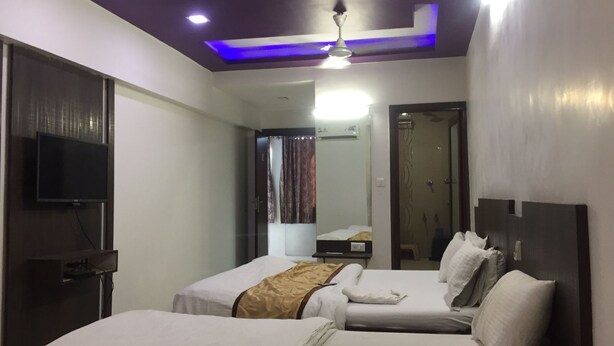 A hotel room with two beds, a flat-screen TV, a ceiling fan, and a bathroom visible through an open door. - Hotel Long Stay (Ahmedabad)