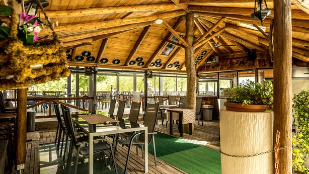 An outdoor wooden deck with tables and chairs, a green artificial turf, and a wooden ceiling with exposed beams. - Hotel Center (Bohinj)