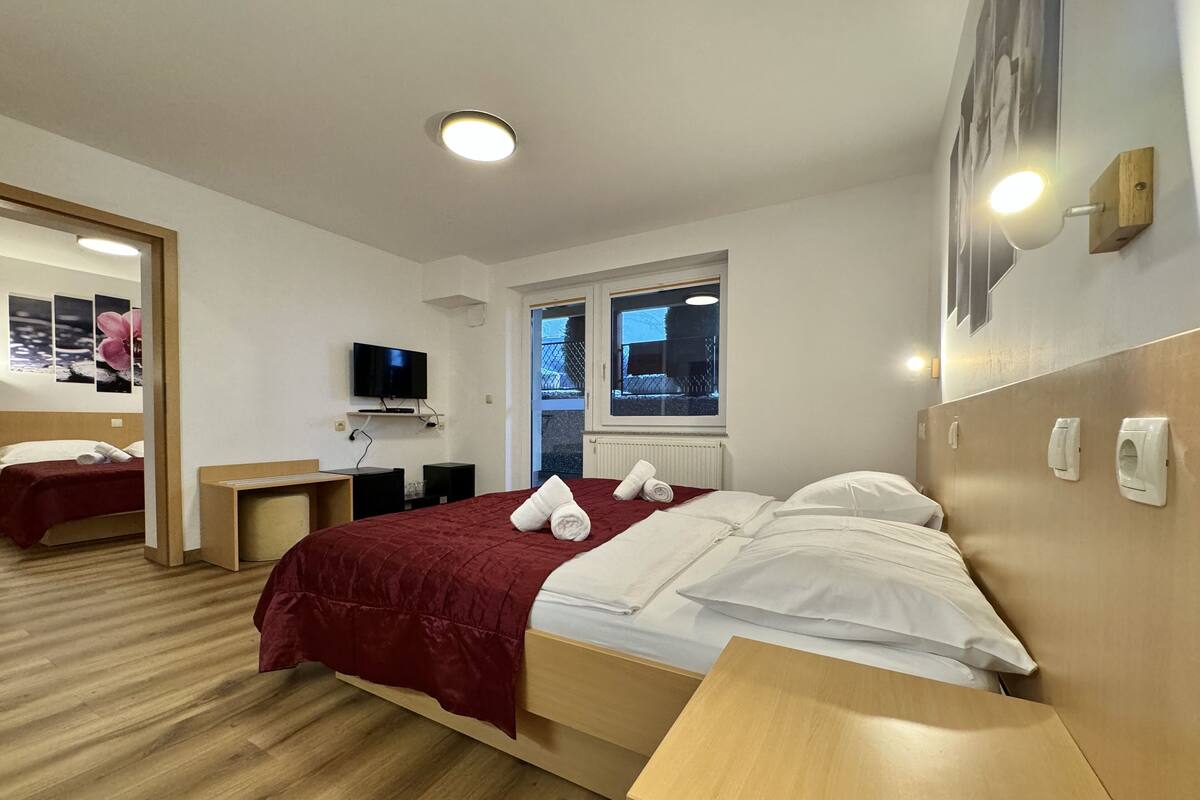 A hotel room with a bed, a TV, a window, and a mirror.