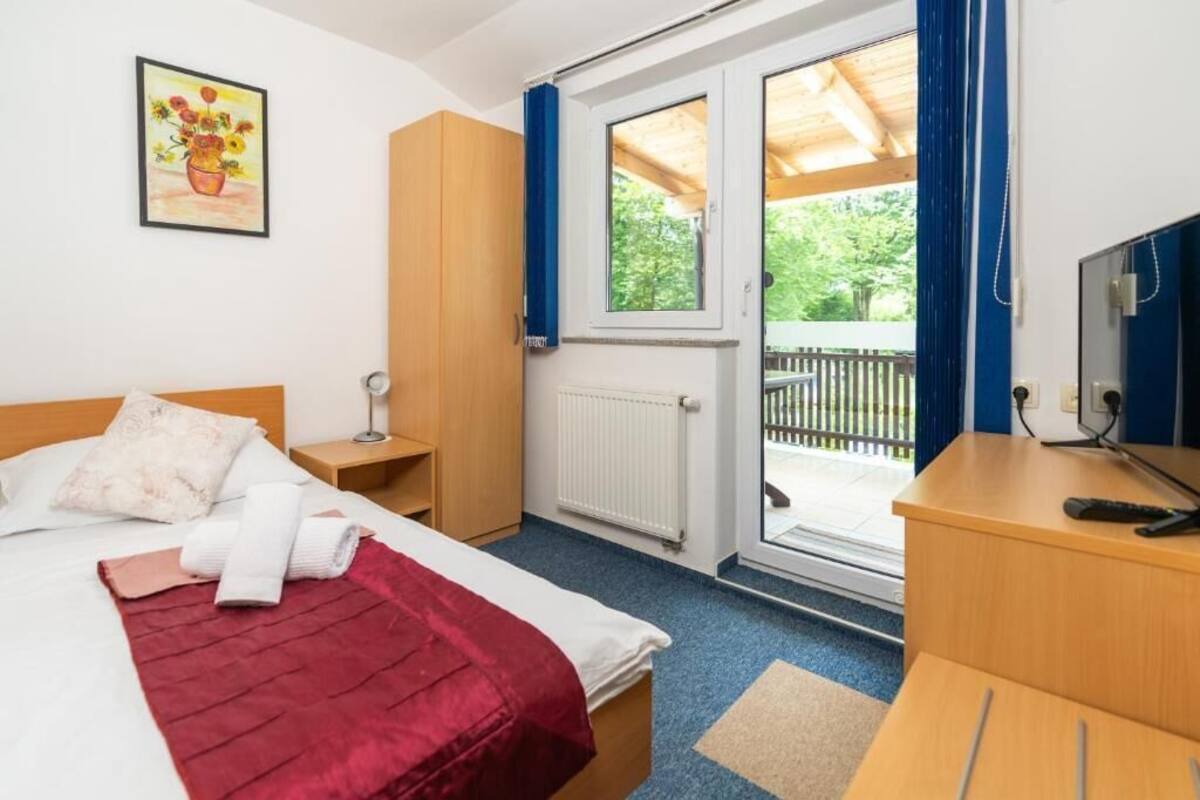 A hotel room with a bed, a desk, a chair, a window, and a door leading to an outdoor area.