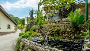 A stone retaining wall with a garden, a wooden building, and a street. - Hotel Center (Bohinj)