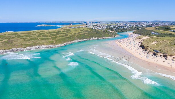 An aerial view of a coastal area with a beach, clear turquoise waters, and a town in the background. - Luxury Newquay home with epic views - dog friendly (Newquay)