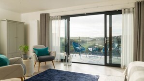 A modern living room with a large sliding glass door leading to a balcony with a view of a landscape and a road. - Luxury Newquay home with epic views - dog friendly (Newquay)