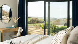 A bedroom with a large sliding glass door leading to a balcony, a wooden desk, a chair, and a bed with a white comforter. - Luxury Newquay home with epic views - dog friendly (Newquay)