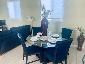 Un coin repas avec une table ronde en verre, des chaises bleu foncé et un vase rempli de fleurs.