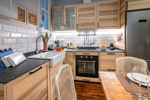 A modern kitchen with wooden cabinets, a black countertop, a sink, an oven, and a dining area with a wicker chair and table.