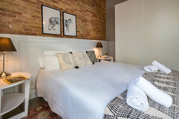 A hotel room with a large bed, two nightstands, a brick wall, and two framed animal prints.