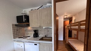 A compact kitchen with a dishwasher, stove, and coffee maker. A wooden bunk bed is visible in the adjacent room. - RESIDENCE 2-234 - Village center apartment, close to the slopes - Wi-Fi - Garage (La Clusaz)