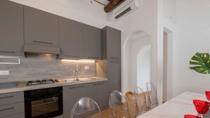 Een moderne keuken met grijze kastjes, een RVS spoelbak en een houten eettafel met transparante stoelen.