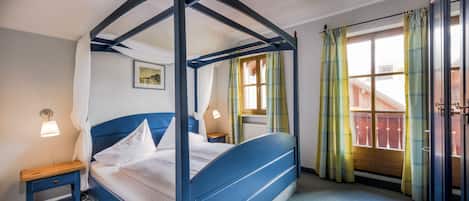 Un lit à baldaquin avec du linge de lit blanc, une table de chevet avec une lampe et une fenêtre avec des rideaux.