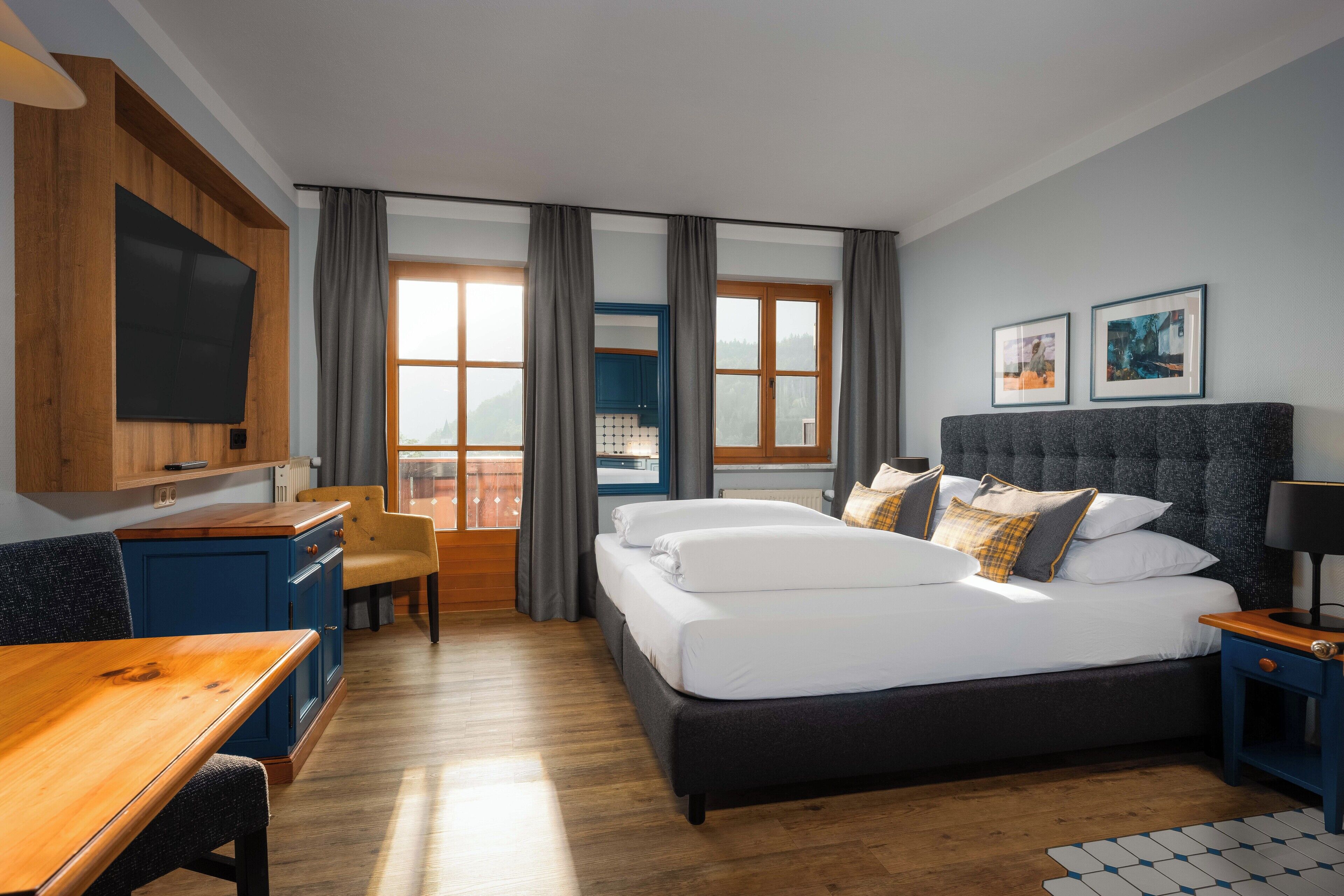 A hotel room with a bed, a desk, a chair, a TV, and a window with curtains.