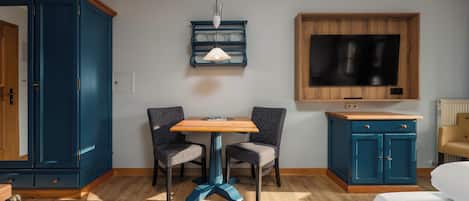 A hotel room with a wooden table, two chairs, a TV mounted on the wall, and a wardrobe.