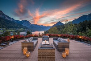 Terraza con mobiliario de mimbre y velas, con vistas a un paisaje montañoso y un lago.