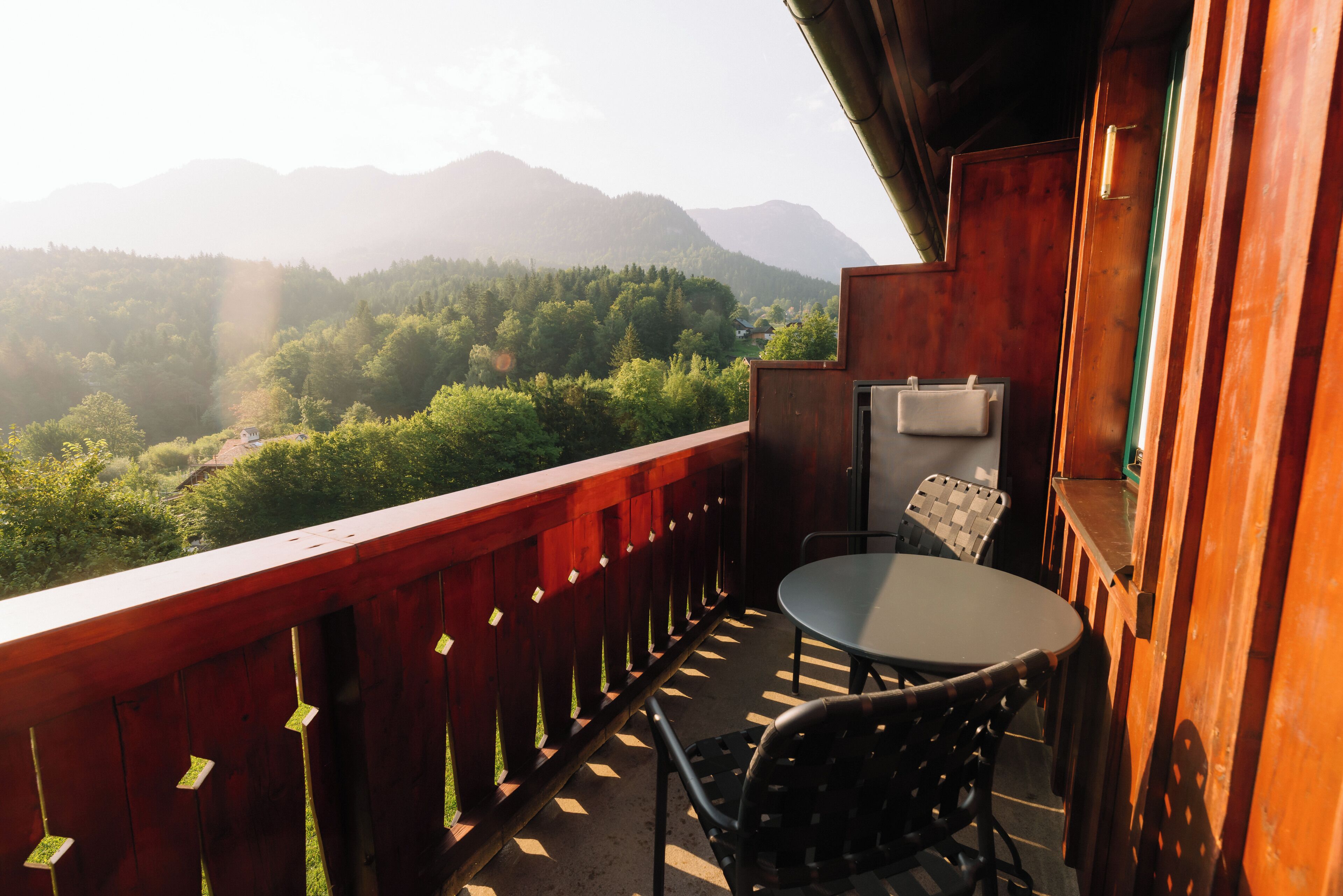 A balcony with a table and chairs, overlooking a forested valley and mountains.