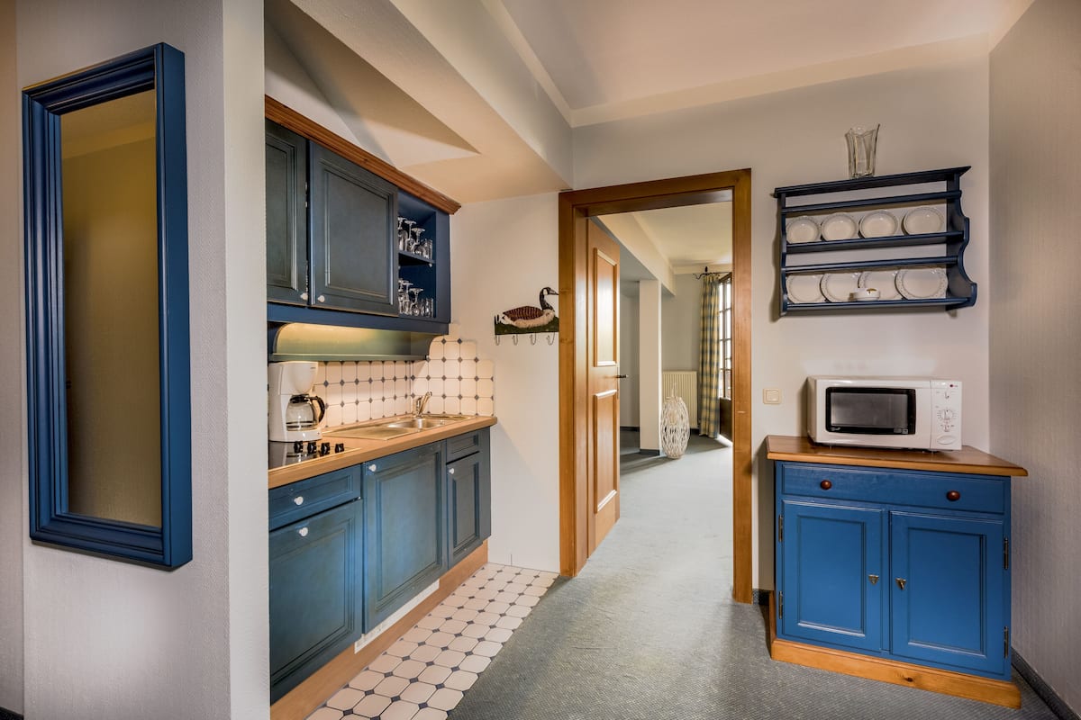 Een smalle keuken met blauwe kastjes, een magnetron op een houten aanrecht en een betegelde achterwand.