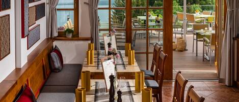 Un comedor con una mesa larga dispuesta para una comida, un sofá con cojines, y vistas al exterior.