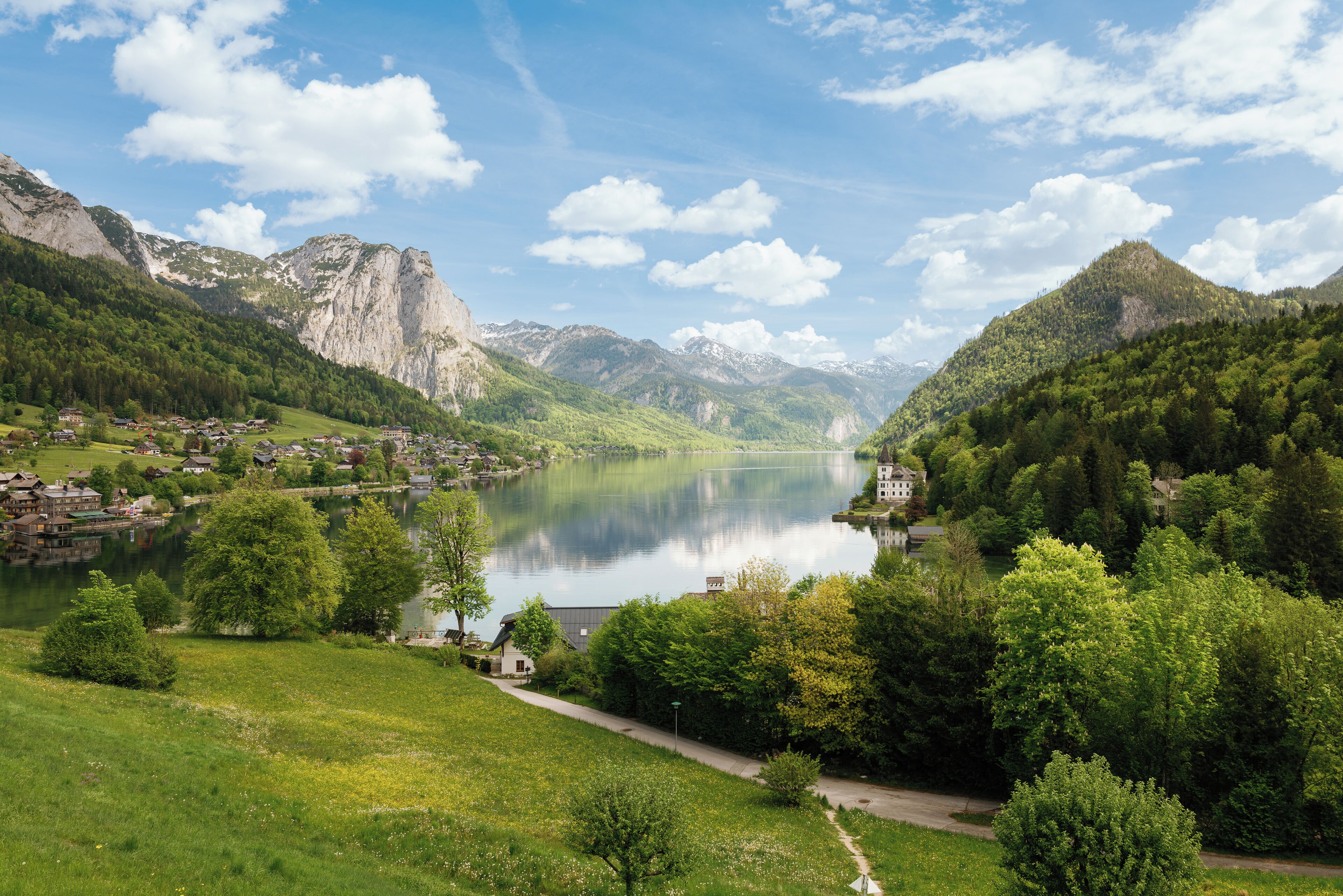 A serene lakeside village with traditional houses, a clear sky, and lush greenery.